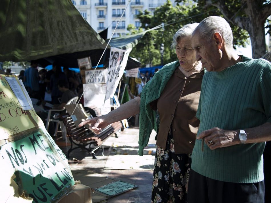 Una pareja visita #acampadavalencia y comenta alguno de los carteles reivindicativos.